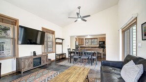Ein Wohnzimmer mit einer schwarzen Ledersofa, einem Holztisch, einem an der Wand montierten Fernseher und einer Küche im Hintergrund.