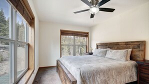 Ein Schlafzimmer mit großem Fenster, Deckenventilator, Holz-Kopfteil und Bett mit weißer Bettdecke.