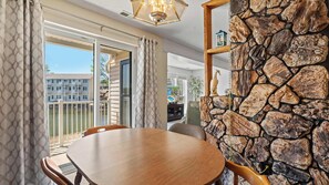 A dining area with a stone wall, a wooden table, and a view of a building through glass doors. - Ozark Get-Away Lakefront Condo with Boat Slip (Osage Beach)