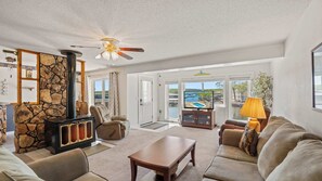 A spacious living room with a stone fireplace, comfortable seating, and large windows offering a view of the outdoors. - Ozark Get-Away Lakefront Condo with Boat Slip (Osage Beach)