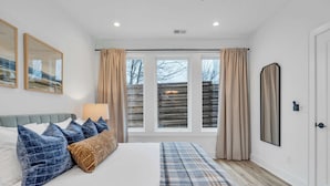 Ein Schlafzimmer mit Bett, Lampe, einem Fenster mit Vorhängen und einer Tür.