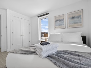 Een slaapkamer met een bed, een raam met uitzicht, een deur en twee foto’s in lijsten aan de muur.