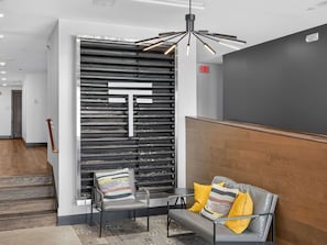Een moderne lobby met een receptiebalie, een zithoek met een bank en stoelen, een decoratieve wand met een groot 'T'-ontwerp, en een houten accentwand.