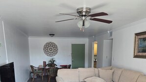 A living room with a sectional sofa, a glass coffee table, a ceiling fan, a dining area with chairs and a table, and a TV stand. - 2-bedroom apartment in amazing Fort Myers with AC (Fort Myers)