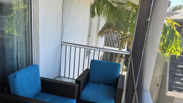 A balcony with wicker furniture and a view of a house and palm trees. - 2-bedroom apartment in amazing Fort Myers with AC (Fort Myers)