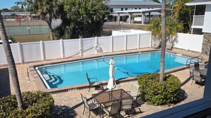 A swimming pool with a white fence, palm trees, and a view of a building in the background. - 2-bedroom apartment in amazing Fort Myers with AC (Fort Myers)