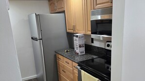 A compact kitchen with a refrigerator, oven, microwave, and wooden cabinets. - 2-bedroom apartment in amazing Fort Myers with AC (Fort Myers)