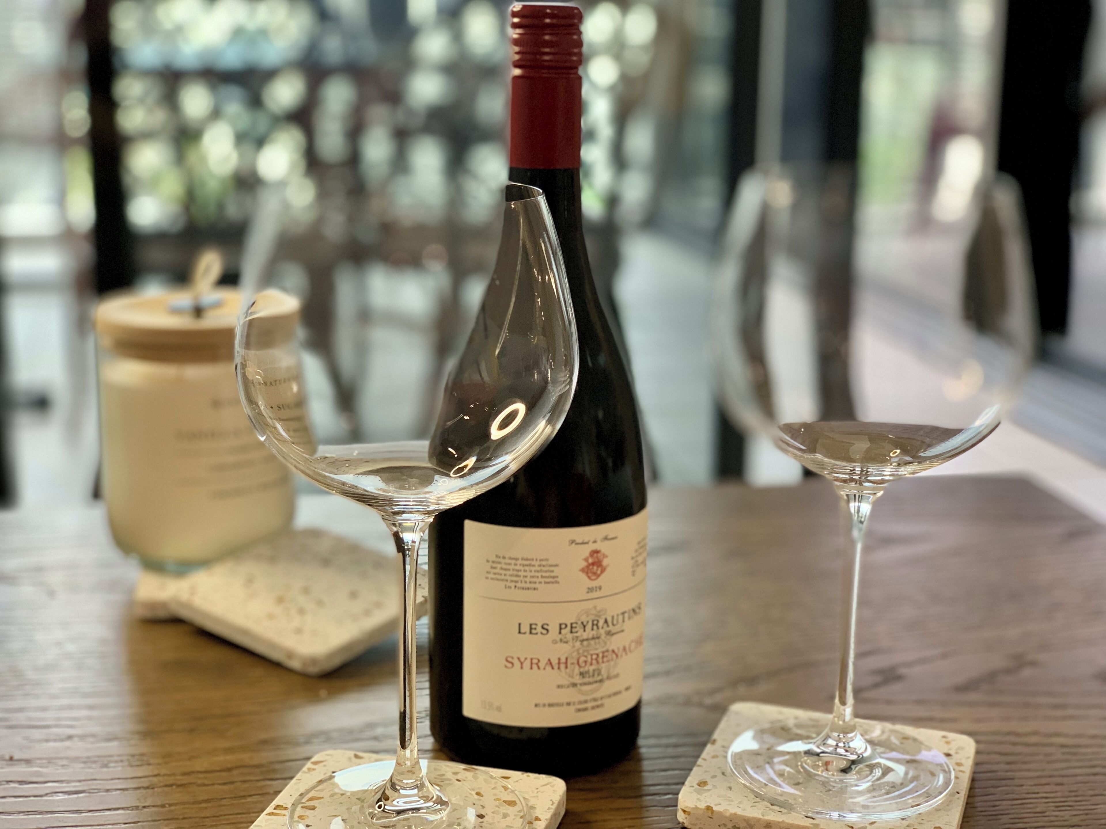 A bottle of wine, two wine glasses, and a jar on a wooden table.