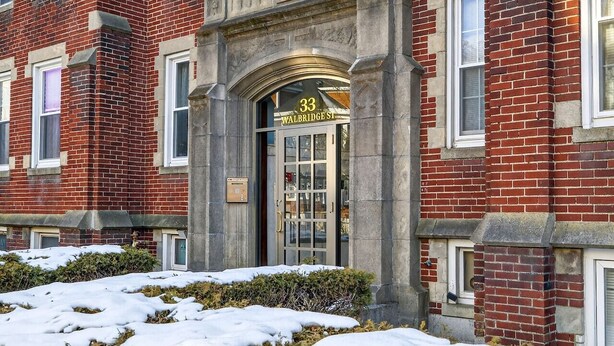 A red brick building with a prominent entrance labeled '33 Walbridge St.' - Allston 1BR Near Green Line | Sleeps 4 (Boston)