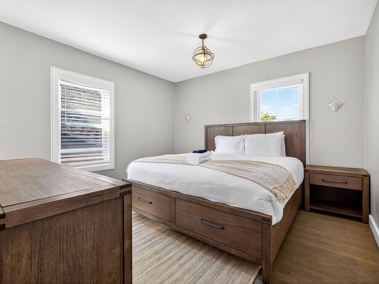 Une chambre à coucher avec un lit en bois, des tables de chevet, un bureau et un luminaire suspendu.
