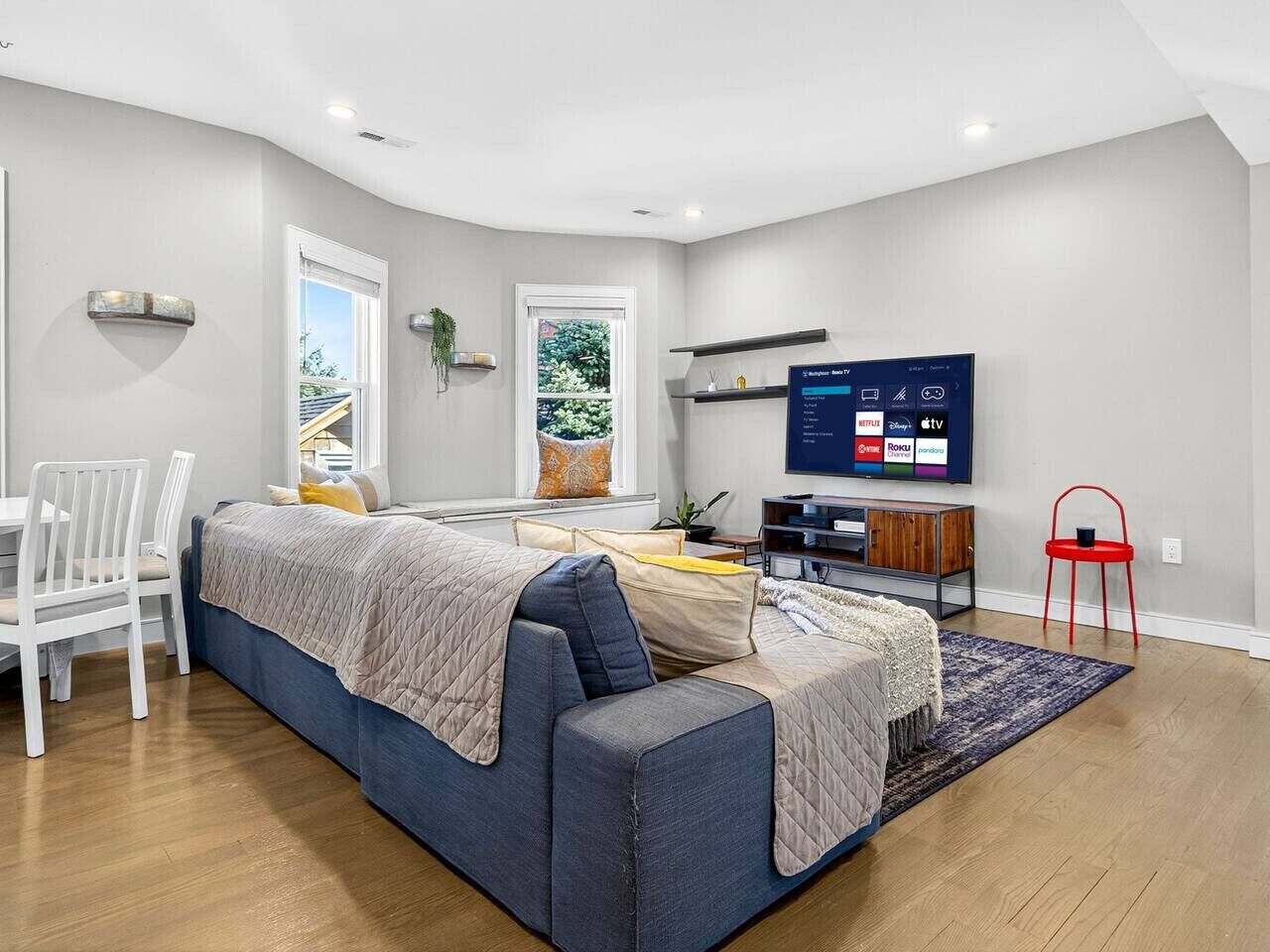 Ein modernes Wohnzimmer mit einer Couch, einem Esstisch mit Stühlen, einem Fernseher und einem roten Sessel.