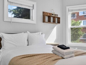A bedroom with a bed, white bedding, a window, and a wooden shelf with a vase. - Luxe 3 bd | Boston | Penthouse (Boston)
