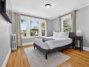 Een moderne slaapkamer met een bed, een radiator, een nachtkastje en een raam met gordijnen.