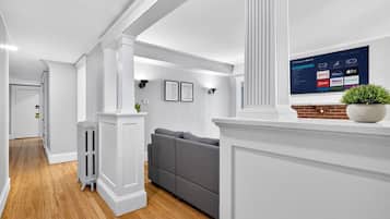 Een moderne woonkamer met een grijze bank, witte zuilen en een tv met streamingdiensten.