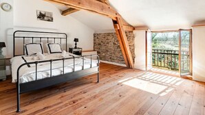 Et soveværelse med metal sengestel, træbjælker, en stenvæg og en balkon med udsigt.