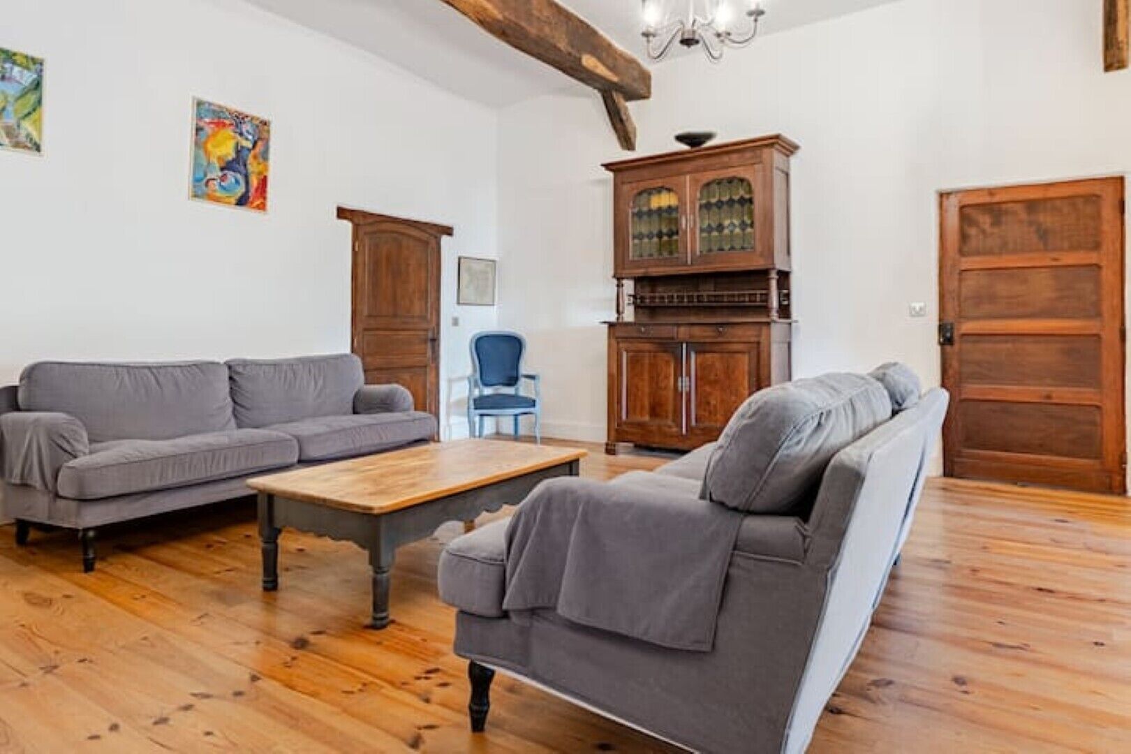 A living room with a grey sofa set, a wooden coffee table, a blue chair, and a cabinet with glass doors.