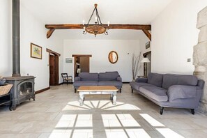 A living room with a fireplace, sofas, a wooden bench, and a chandelier. - Beautiful Villa with Pool + Garden near Biarritz (Auterrive)