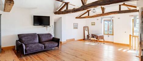 A spacious room with wooden beams, a sofa, a piano, and a TV.