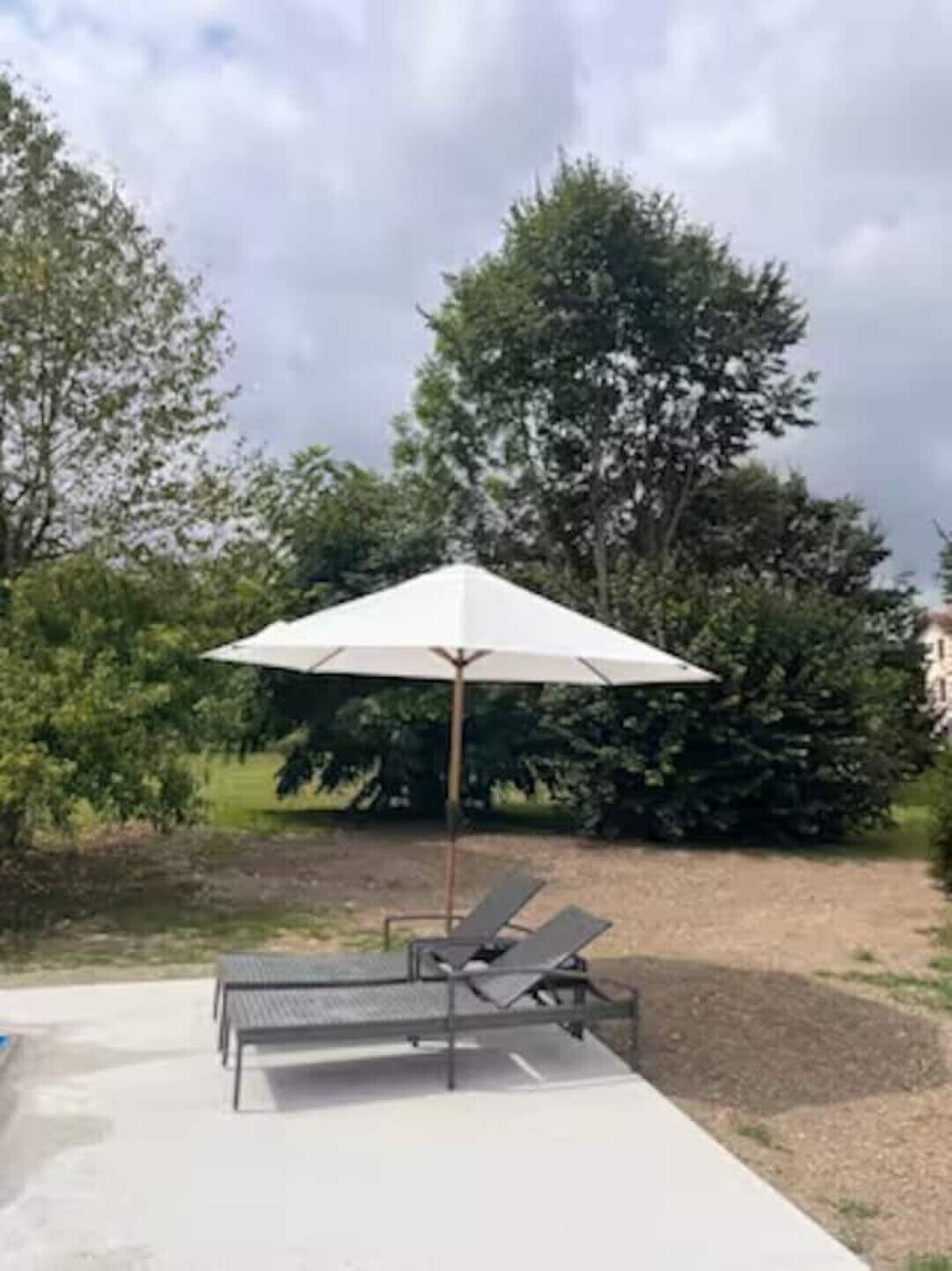 A poolside area with a lounge chair and umbrella, surrounded by trees and a clear sky.