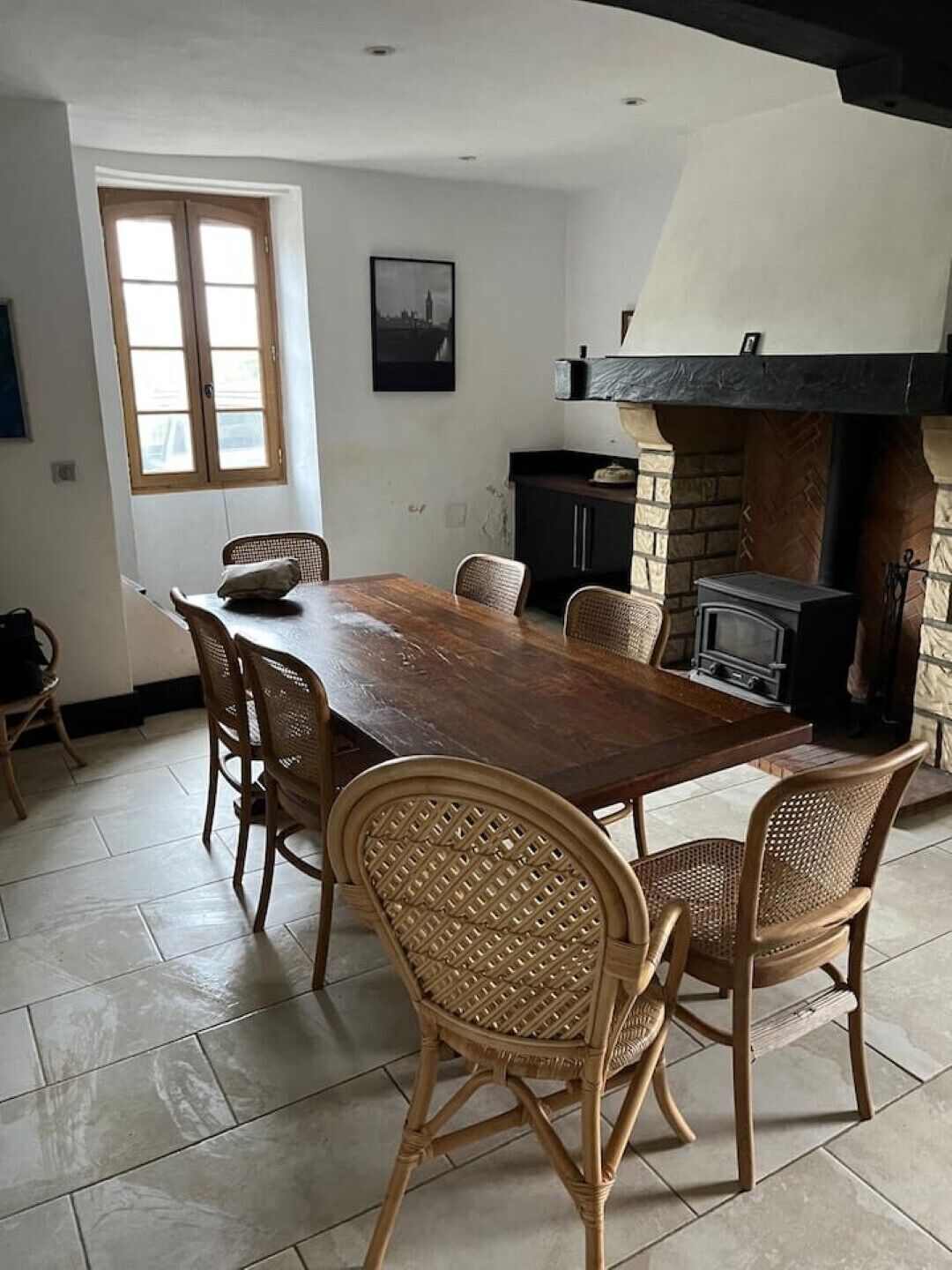 A dining area with a wooden table and wicker chairs, a fireplace, and a window with blinds.
