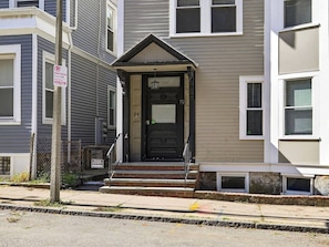 A two-story building with a black front door, a small porch, and a mailbox. - NEW! LUX 3BR w/ 400 Mbps Wifi | ROKU TV & Games! (Boston)