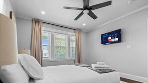 A bedroom with a bed, a ceiling fan, a TV, and a window with curtains.