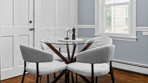 A room with a round glass table, four chairs, a door, and a window with blinds.