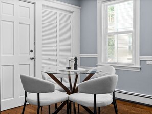 A room with a round glass table, four chairs, a door, and a window with blinds.