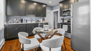 A modern kitchen with dark cabinets, a stainless steel refrigerator, and a round glass table with chairs.