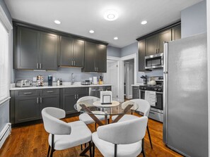 A modern kitchen with dark cabinets, a stainless steel refrigerator, and a round glass table with chairs.
