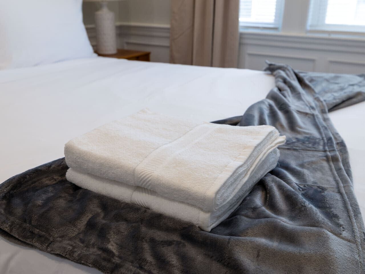 Un lit bien fait, avec une serviette blanche pliée et une couverture gris foncé.