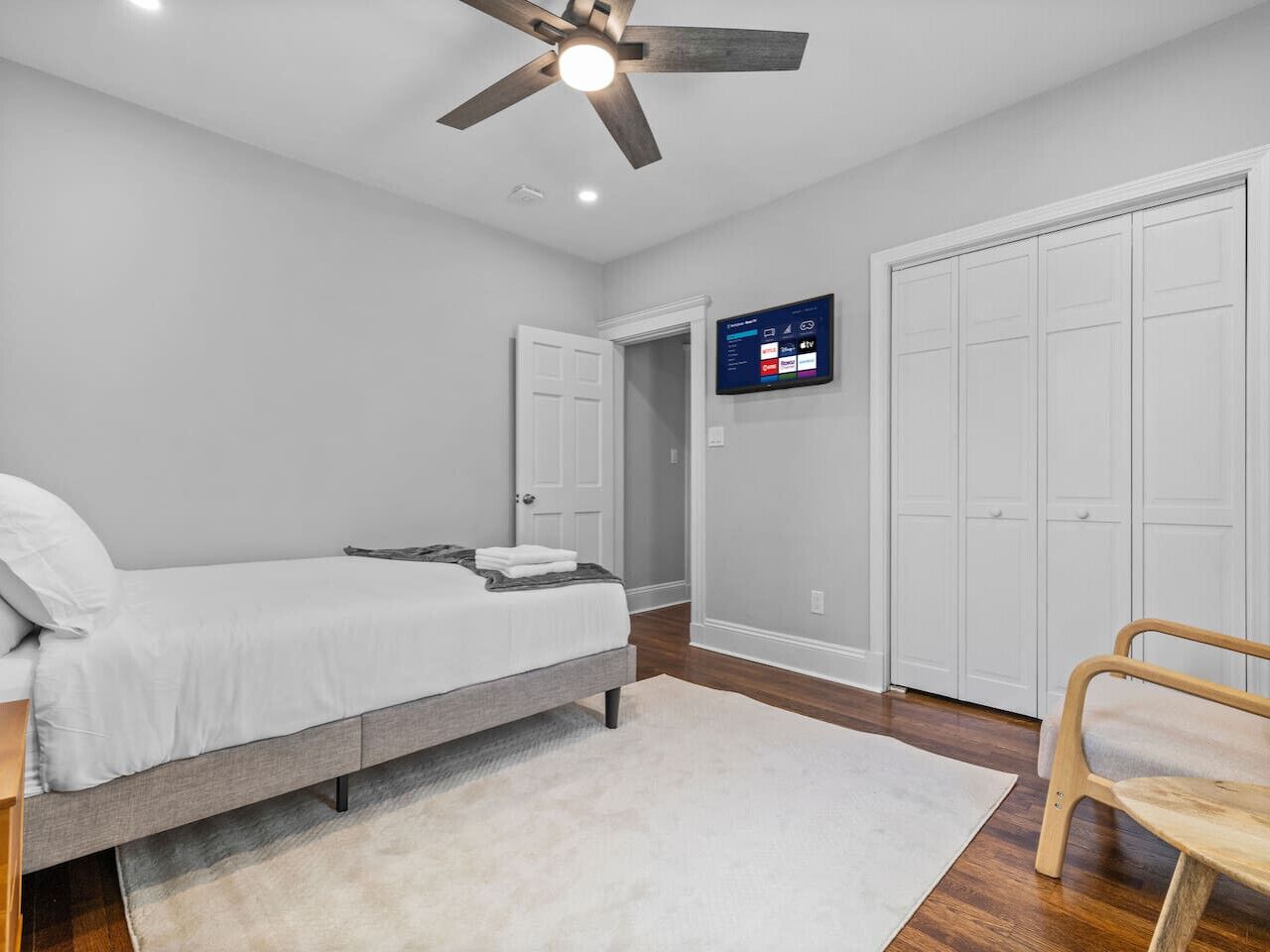 A bedroom with a bed, a ceiling fan, a TV mounted on the wall, and a wardrobe.