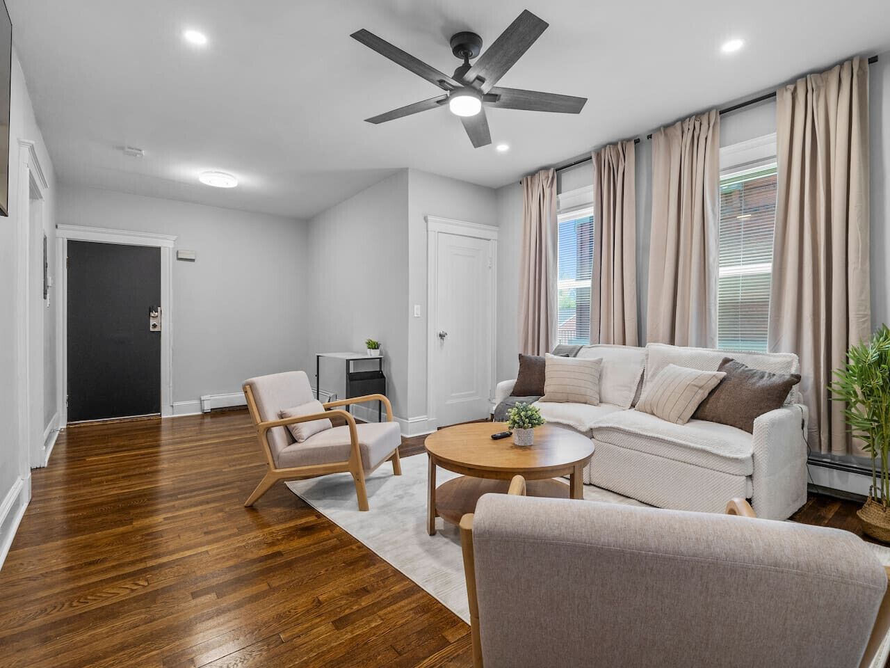 A modern living room with a ceiling fan, a sofa, two armchairs, a coffee table, and a potted plant.
