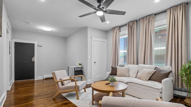 A modern living room with a ceiling fan, a sofa, two armchairs, a coffee table, and a potted plant.