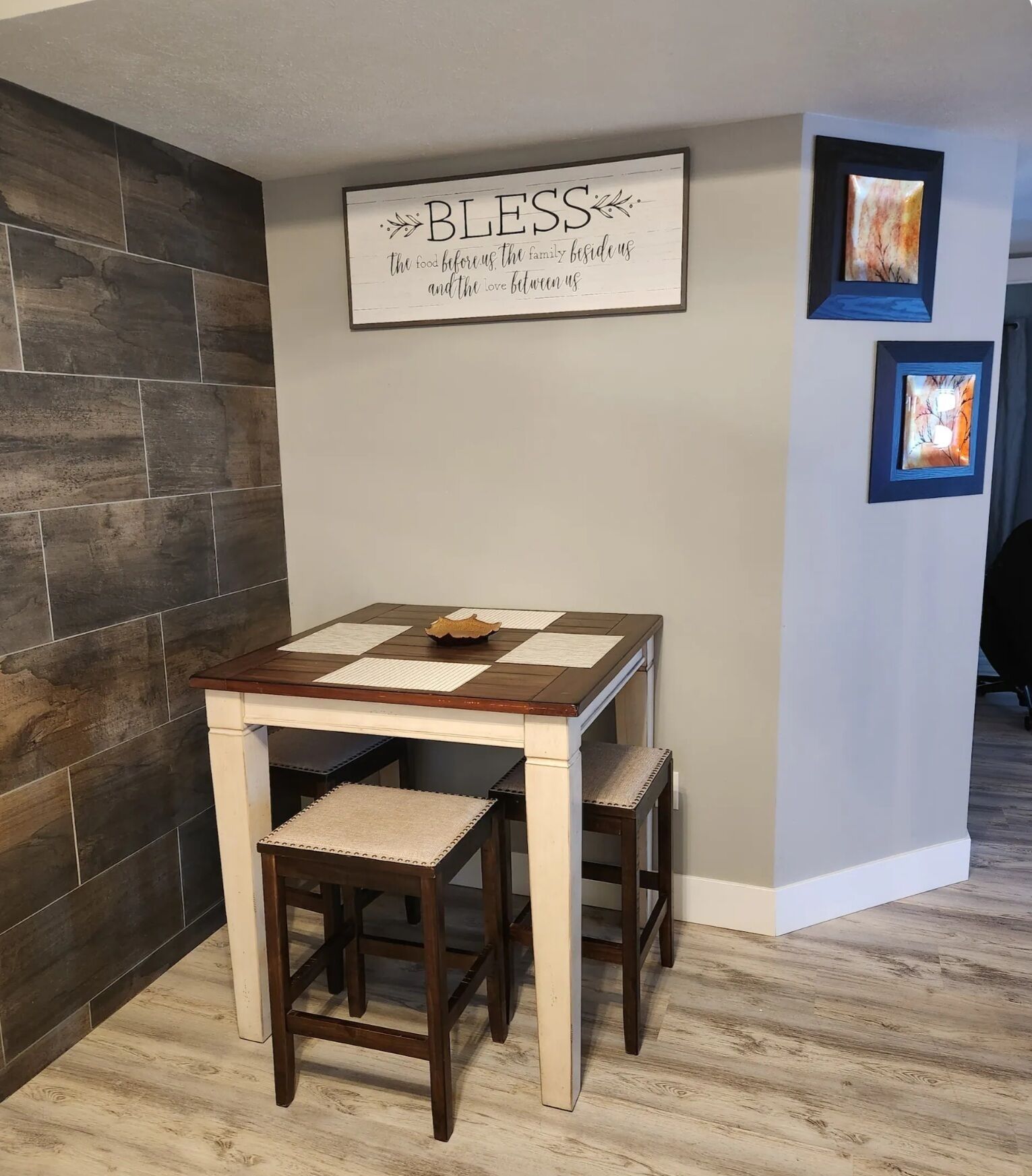 Un comedor con una mesa y sillas de madera, un letrero en la pared y obras de arte enmarcadas.