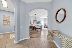 A spacious hallway with a dining area in the background, a round mirror on the wall, and patterned rugs on the floor. - Modern Vista Cay Condo Walk to Pool 3 Min to OCCC & Epic Park (Orlando)