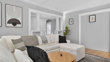 Een moderne woonkamer met een hoekbank, een ronde salontafel en kunstwerken in lijsten aan de muren.