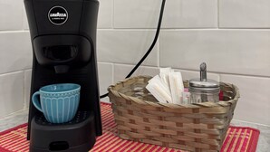 Eine Kaffeemaschine auf einer roten Matte, ein Korb mit Servietten und eine Wandsteckdose.