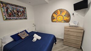 Ein Schlafzimmer mit einem Bett, einer Kommode, einem Fernseher und zwei Kunstwerken an den Wänden.