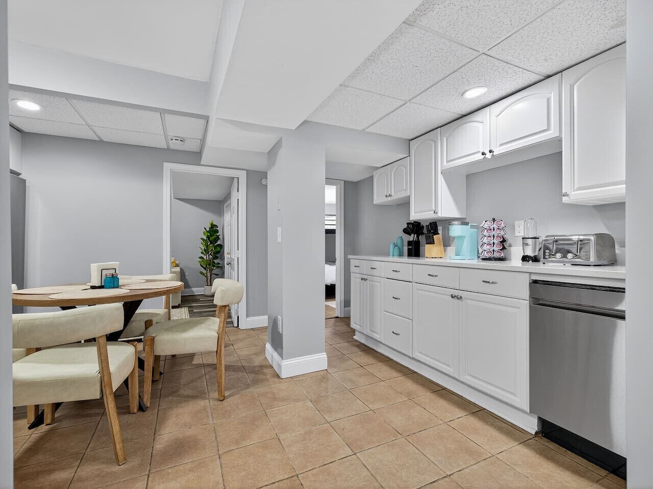 A modern kitchen with white cabinets, a dining area with a table and chairs, and a visible refrigerator.