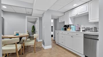 A modern kitchen with white cabinets, a dining area with a table and chairs, and a visible refrigerator.