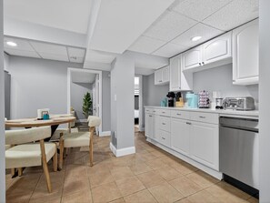 Eine moderne Küche mit weißen Schränken, ein Essbereich mit Tisch und Stühlen sowie ein sichtbarer Kühlschrank.