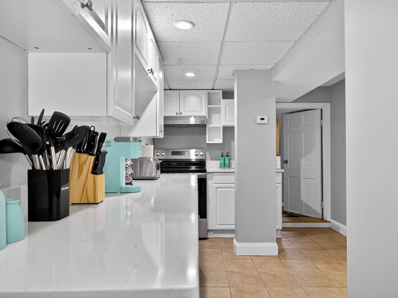 Una cocina moderna con armarios blancos, un refrigerador de acero inoxidable y una encimera con utensilios de cocina.