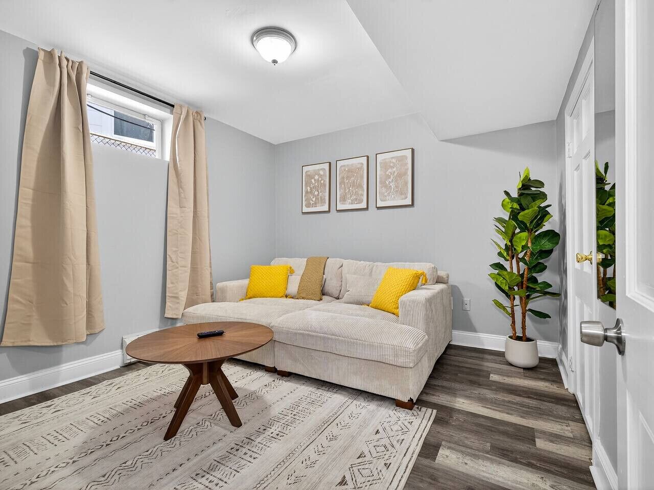 A living room with a sofa, a round coffee table, a potted plant, and a window with curtains.