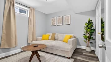 A living room with a sofa, a round coffee table, a potted plant, and a window with curtains.