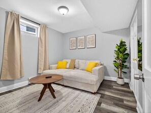Ein Wohnzimmer mit einer Couch, einem runden Couchtisch, einer Topfpflanze und einem Fenster mit Vorhängen.