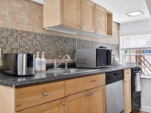 A modern kitchen with a stainless steel microwave, toaster, and dishwasher, wooden cabinets, and a tiled backsplash.