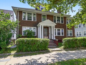 A two-story brick house with a front porch, a staircase, and a well-maintained lawn.