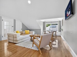 A modern living room with a sofa, armchairs, a coffee table, and a TV mounted on the wall.
