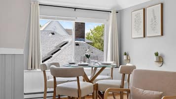 A dining area with a table and chairs, a window with curtains, and two framed botanical illustrations on the wall.